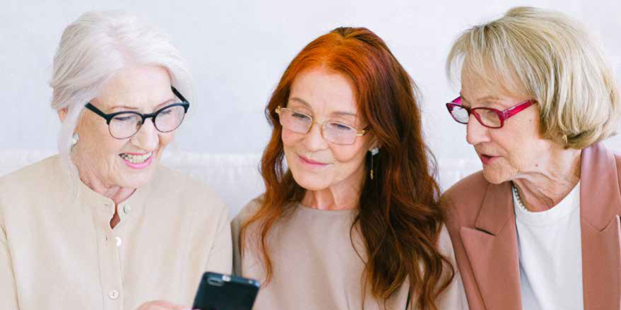 Drei Seniorinnen nehmen an einem Handykurs teil, um Tipps und Informationen zur Handynutzung zu erhalten
